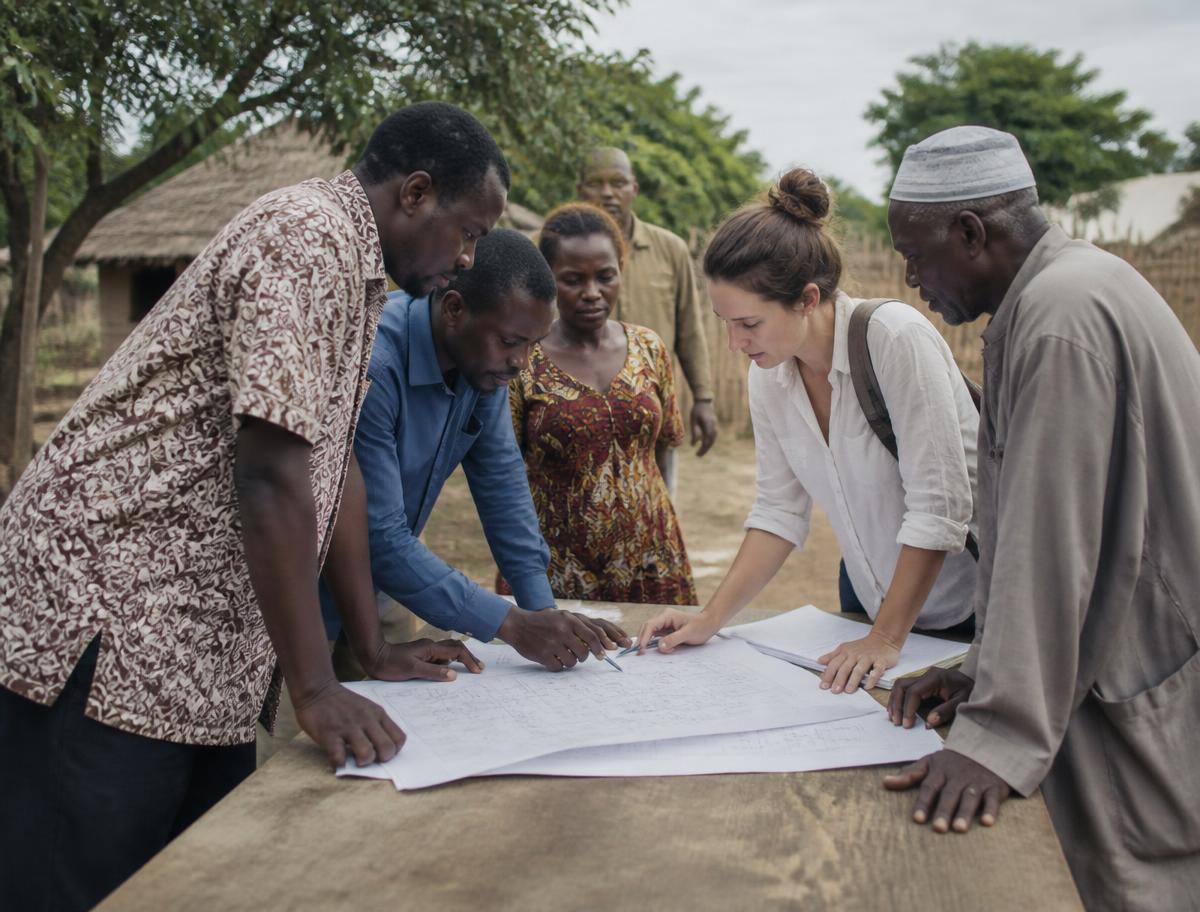 Field workers and community members reviewing plans on a table in a village