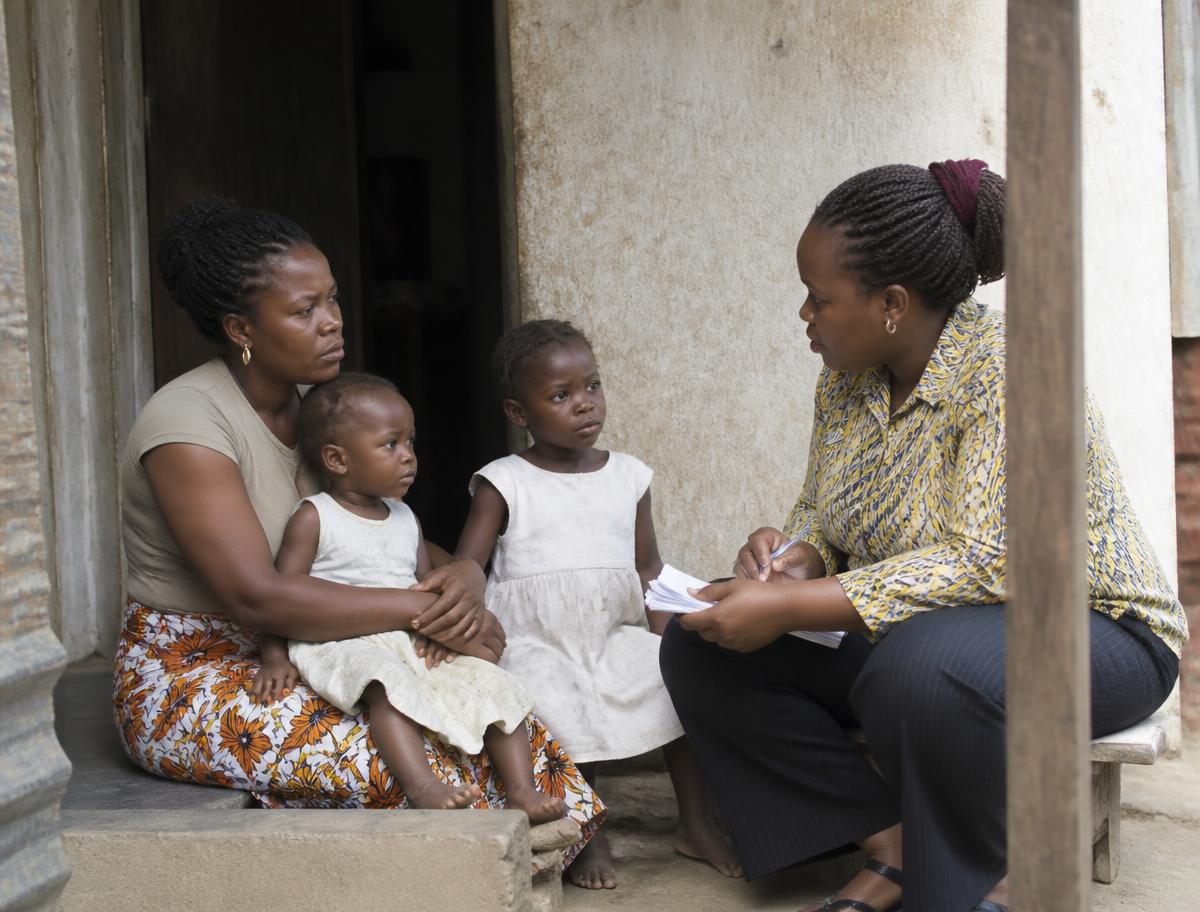 A case worker talking with a mother and her two young children outside their home