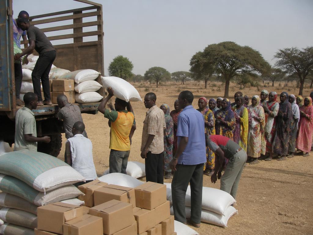 Volunteers unloading sacks and boxes of relief supplies from a truck as people queue